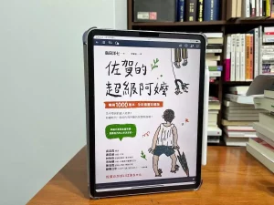 這日一張在書櫃前的原木書桌，書桌上立著一個iPad Pro，螢幕上是日本作家島田洋七創作的佐賀的超級阿嬤的繁體中文電子書封面