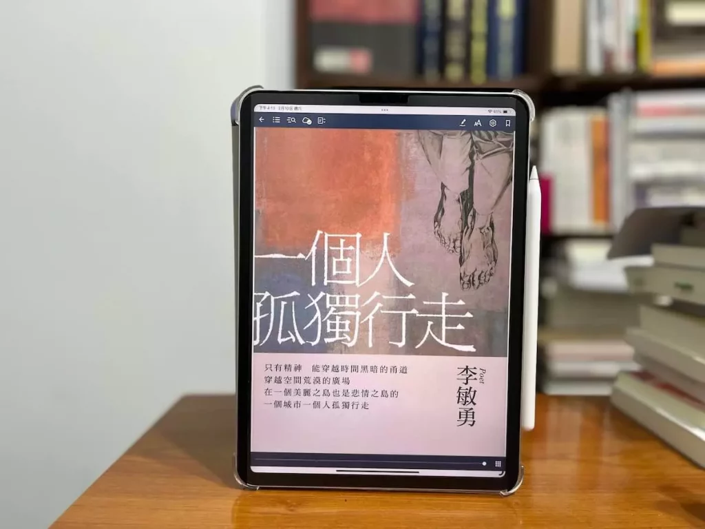 這日一張在書櫃前的原木書桌，書桌上立著一個iPad Pro，螢幕上是臺灣詩人李敏勇創作的詩集《一個人孤獨行走》的電子書封面