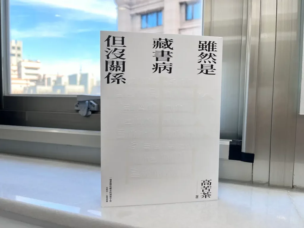 這是一本立在窗邊白色大理石窗台上的紙本書，書後有窗映照著青藍漸層的天，一抹白雲，紙本書是作家高苦茶的著作雖然是藏書病但沒關係